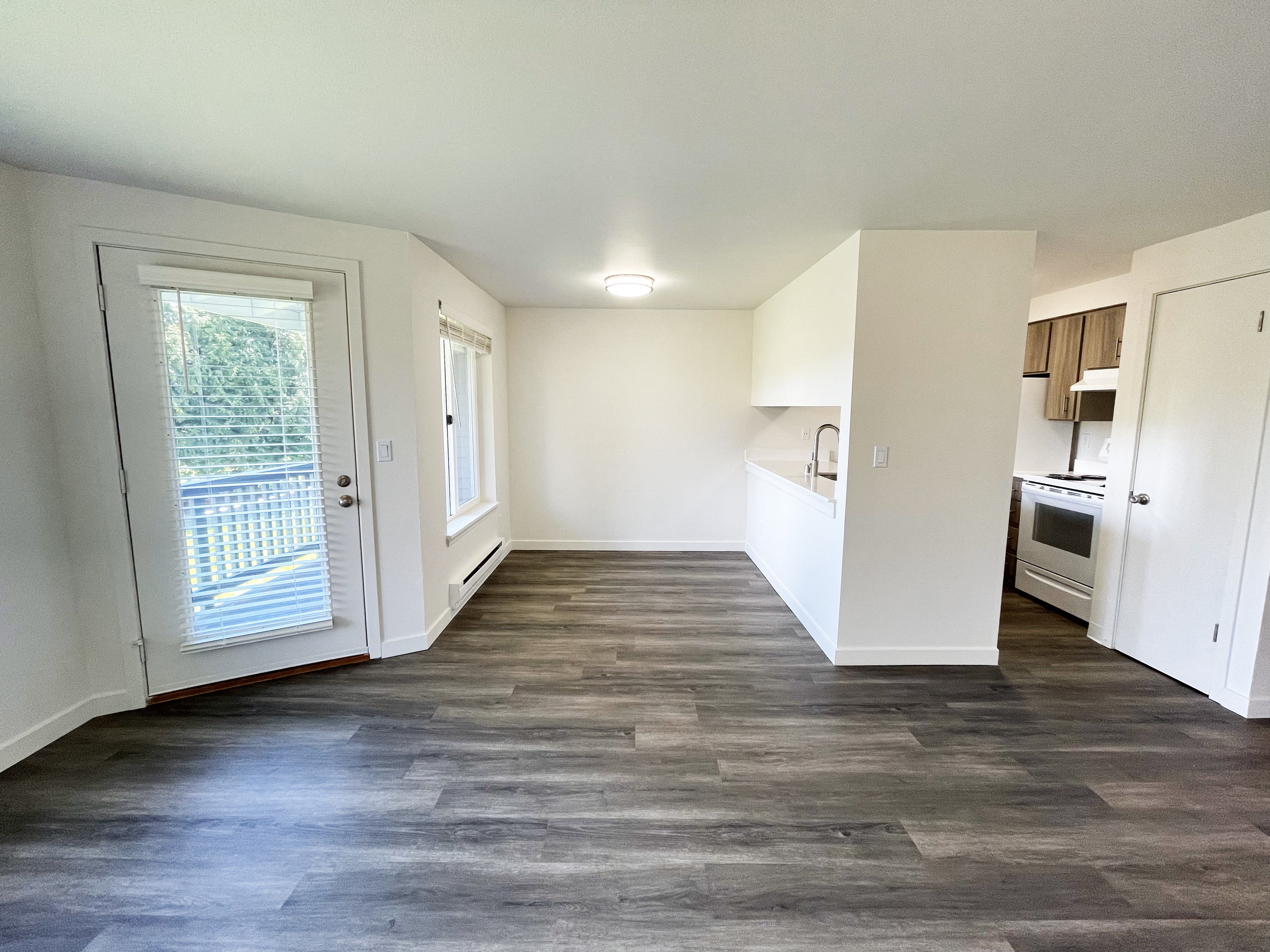 an empty living room and kitchen with white walls and wood flooring